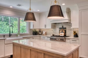 Open kitchen with a wood island base, white cabinetry, marble-look countertops, and black-and-gold pendant lighting.