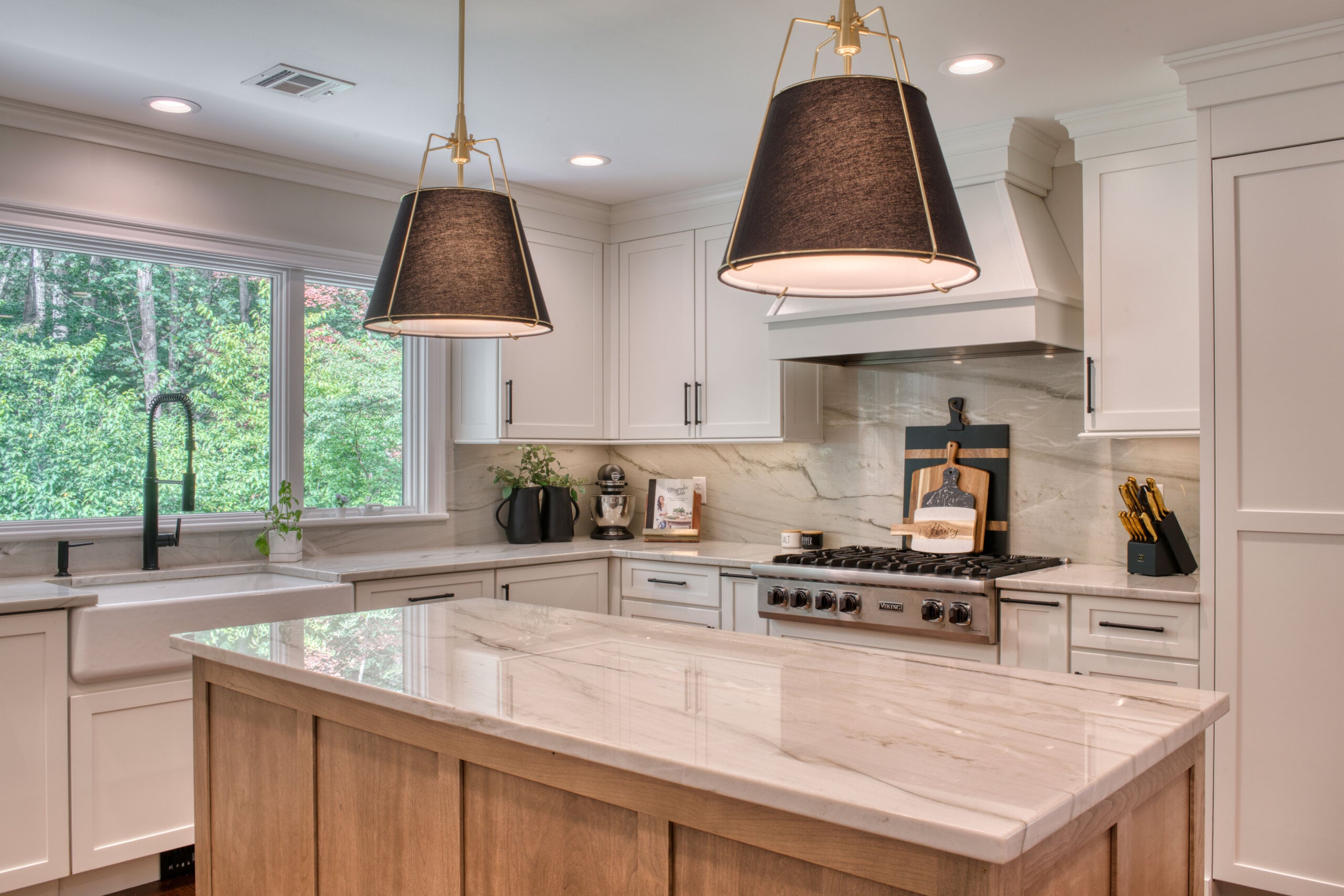 Open kitchen with a wood island base, white cabinetry, marble-look countertops, and black-and-gold pendant lighting.