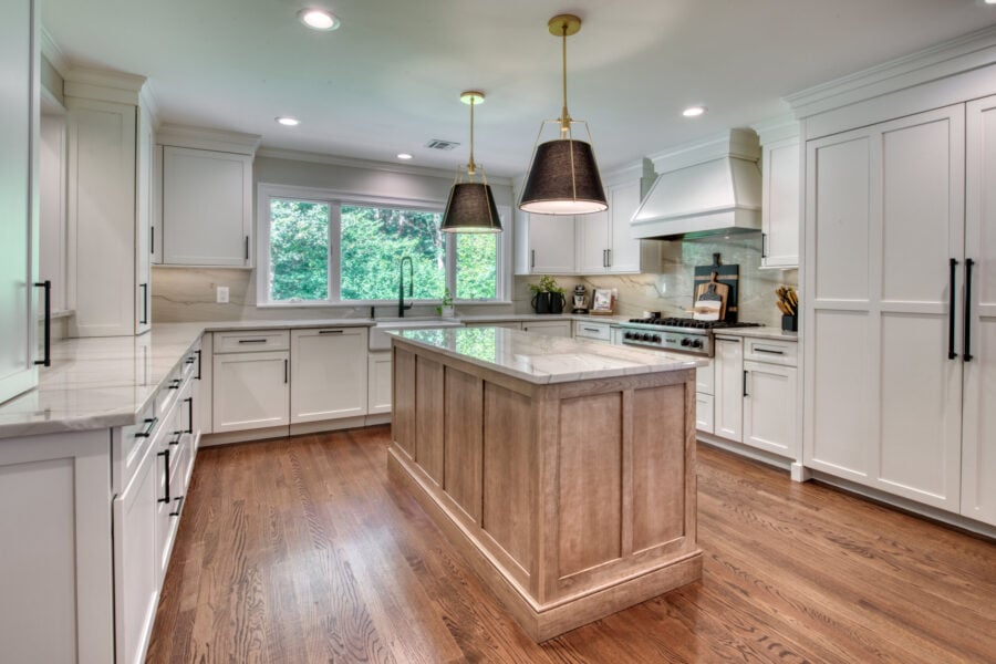 Kitchen with a warm wood island, white shaker cabinets, marble-look counters, and black pendant lights above the island.