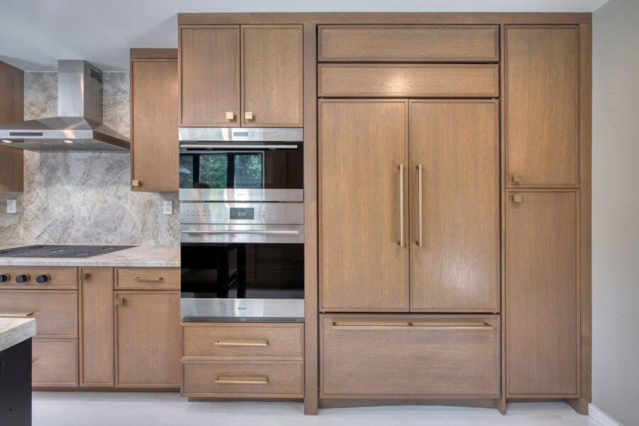 Tall wall of integrated kitchen appliances and panel‑ready refrigerator surrounded by rift‑cut oak cabinetry.