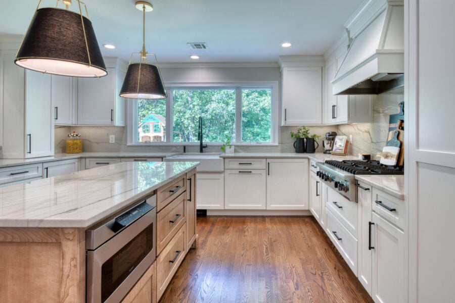 Spacious kitchen with shaker cabinetry, a large island, marble-look countertops, and wide windows overlooking a green backyard.