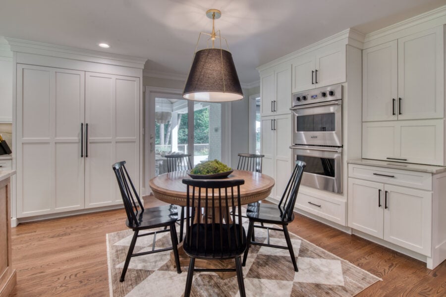Breakfast nook with a round wood table, four black spindle chairs, and surrounding white cabinetry with integrated appliances.