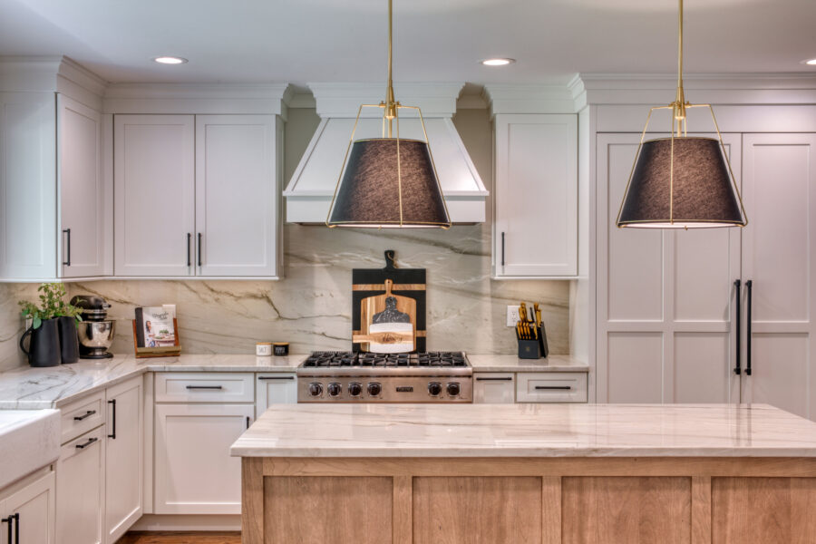 Kitchen range wall featuring white cabinets, a stainless gas cooktop, wood cutting boards, and two large black-and-gold pendant lights over the island.