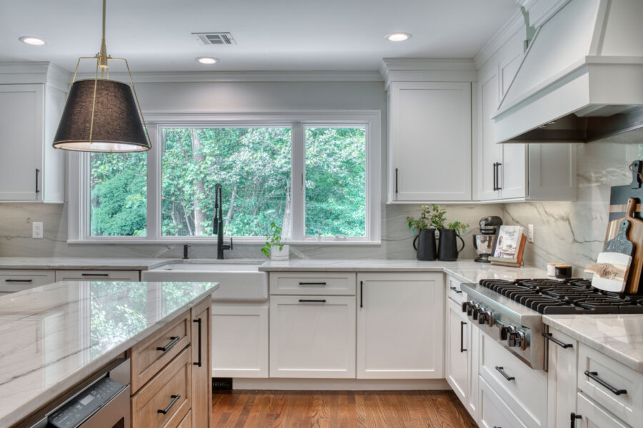 Kitchen sink wall with large windows, a black pull-down faucet, and white shaker cabinetry with marble-look surfaces.