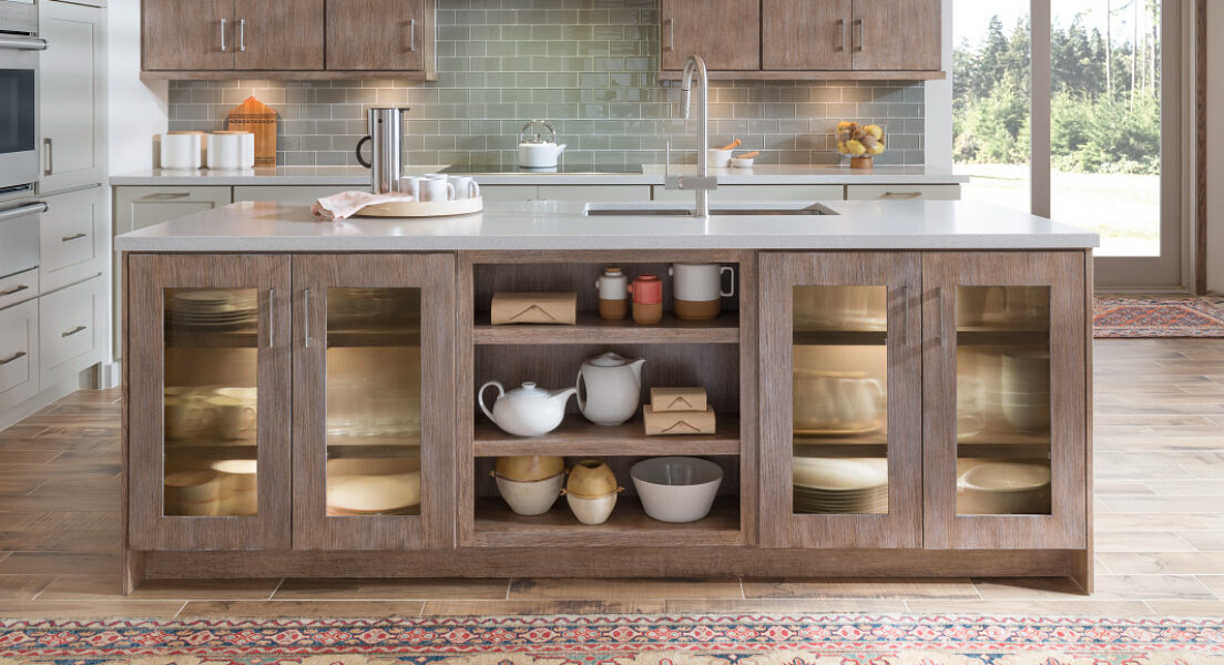 Contemporary kitchen island with open storage shelves, glass-front cabinets, and sleek wood cabinetry paired with a white countertop.