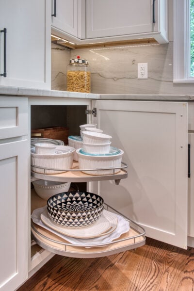 Blind corner kitchen cabinet with pull-out shelves displaying stacked white and patterned bowls.