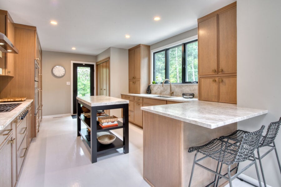 Bright galley‑style kitchen featuring rift‑cut oak cabinets, a large island, and expansive windows overlooking greenery.