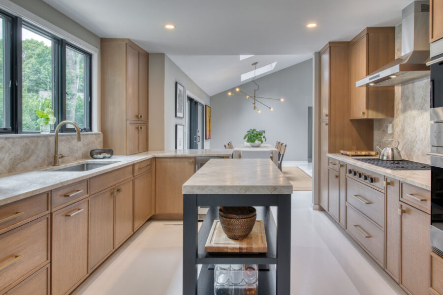 Open‑concept kitchen with rift‑cut oak cabinetry, long island, stone countertops, and a view into the dining area with modern lighting.