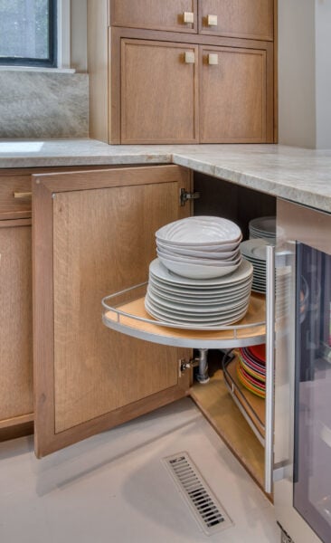 Blind‑corner base cabinet with a rotating pull‑out shelf storing stacked dishes inside a rift‑cut oak kitchen.