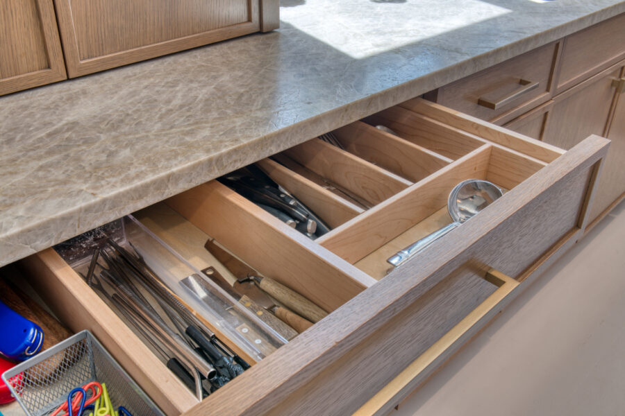 Open kitchen drawer with customizable wood cutlery dividers storing utensils and kitchen tools.