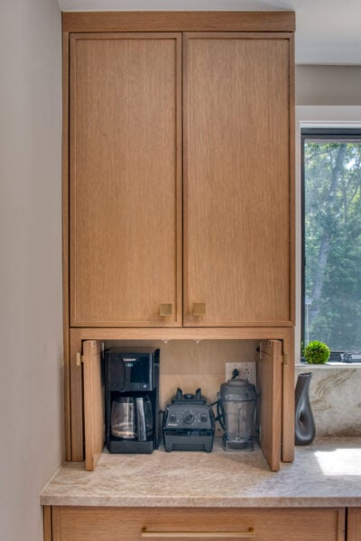 Built‑in appliance garage with rift‑cut oak cabinetry featuring a coffee maker, blender, and mixer stored neatly behind lift‑up doors.