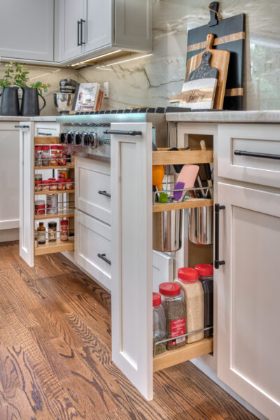 Pull-out base cabinet organizers storing spices, utensils, and kitchen tools beside a stainless gas range.